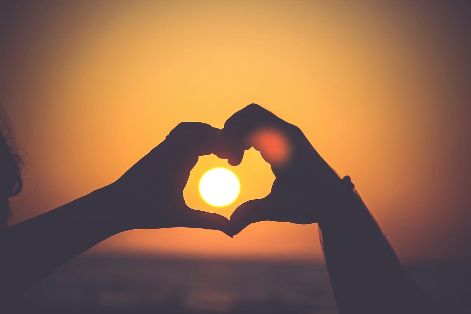 Manos formando la silueta de un corazón, a contraluz de un atardecer