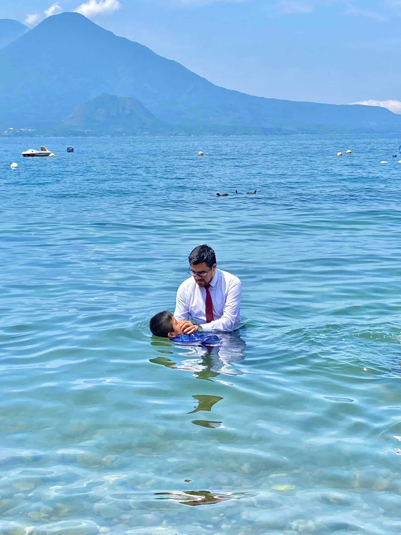 Anthony Araujo bautizando a una persona en un lago, con un volcán al fondo.